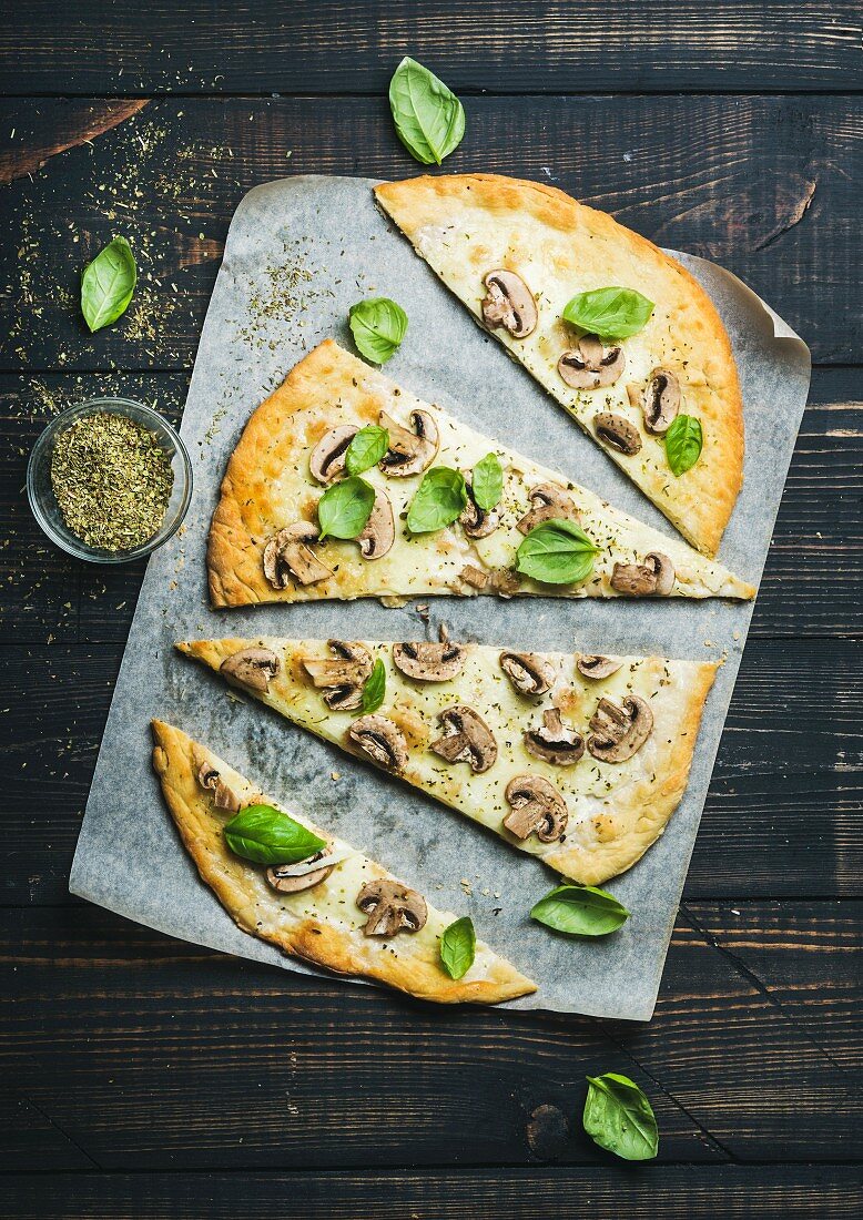 Homemade mushroom pizza with basil cut in slices and spices in glass on baking paper
