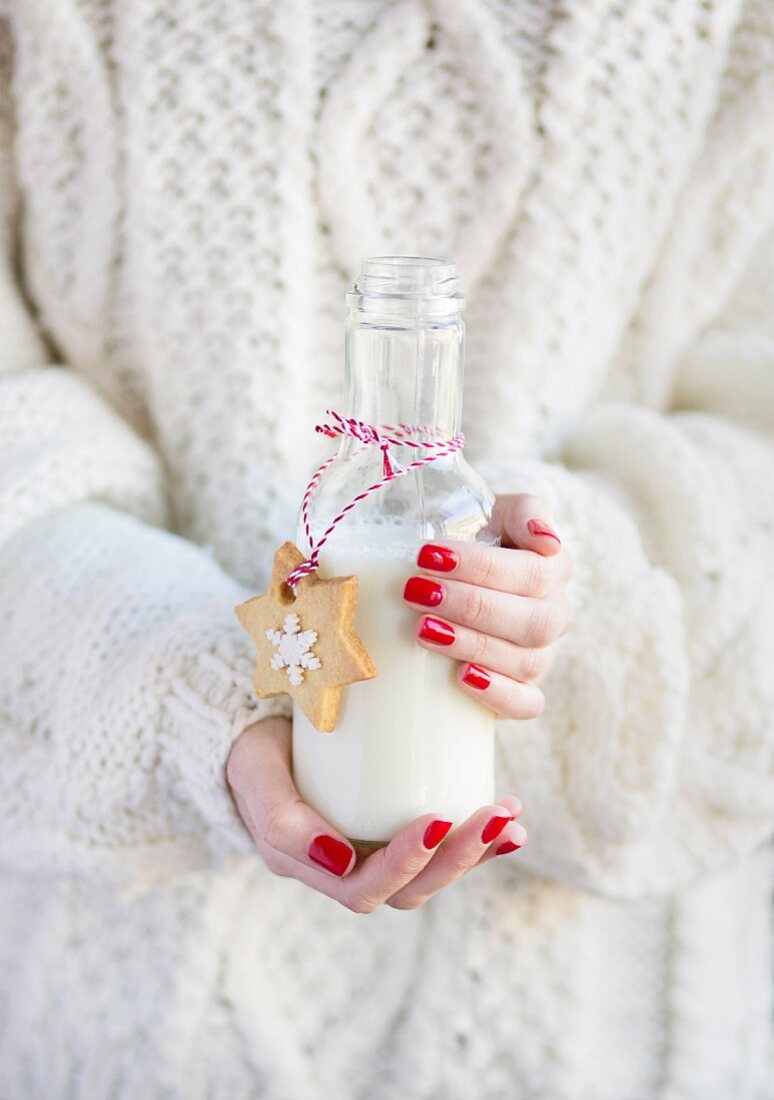 Frau hält eine Flasche Milch mit einem Weihnachtsplätzchen
