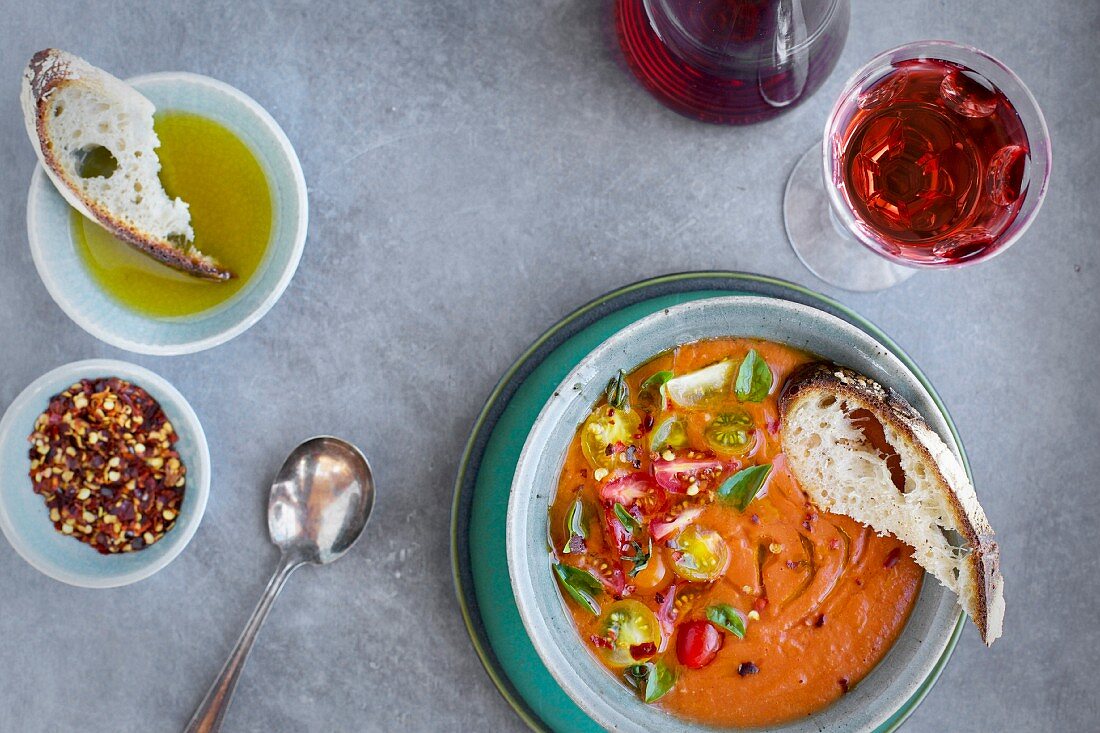 Roasted Tomato Herb Soup topped with cherry tomatoes and basil, served in ceramic bowls served with rose wine, bread and olive oil