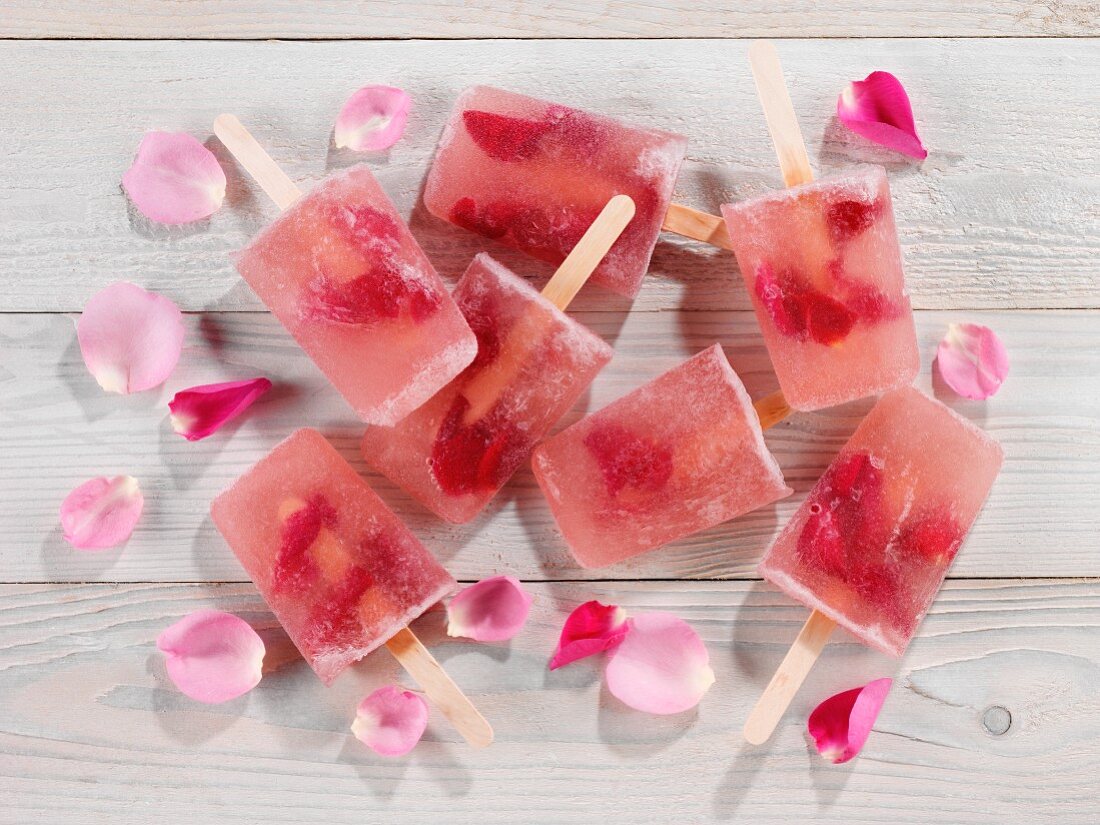 Mehrere Rosenblüten-Eislutscher mit Rosenblättern auf Holzuntergrund