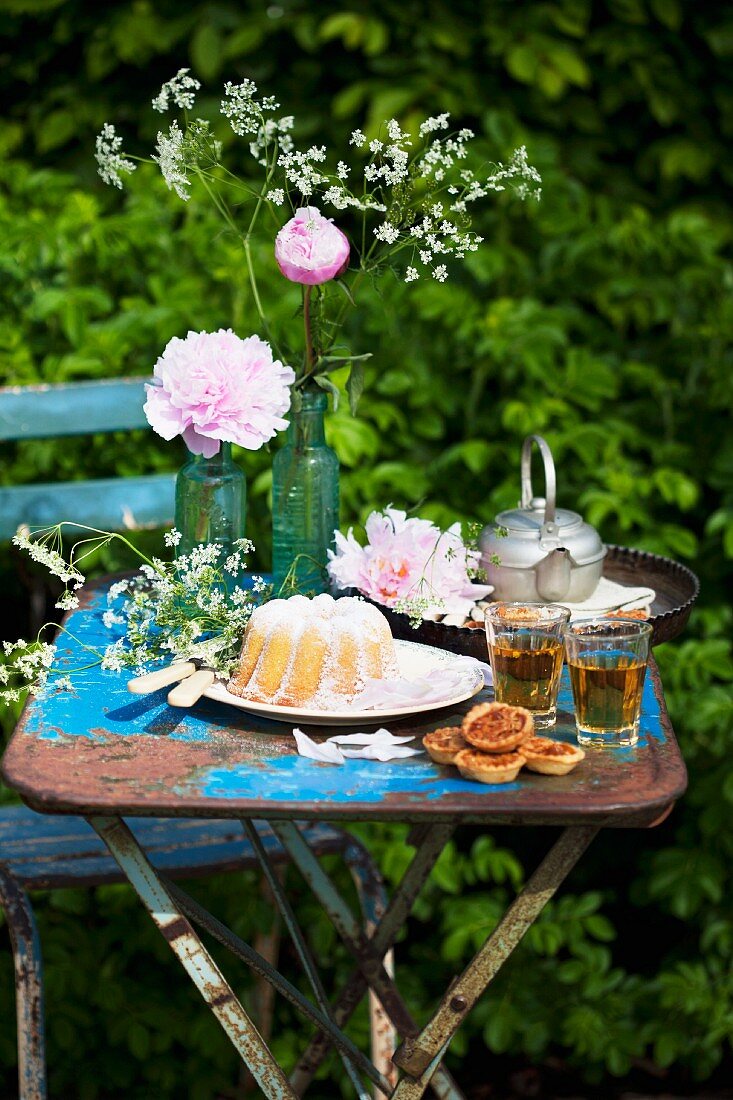 A garden table with peonies, a 'Gugelhupf' ring cake with candles and springtime herb tea