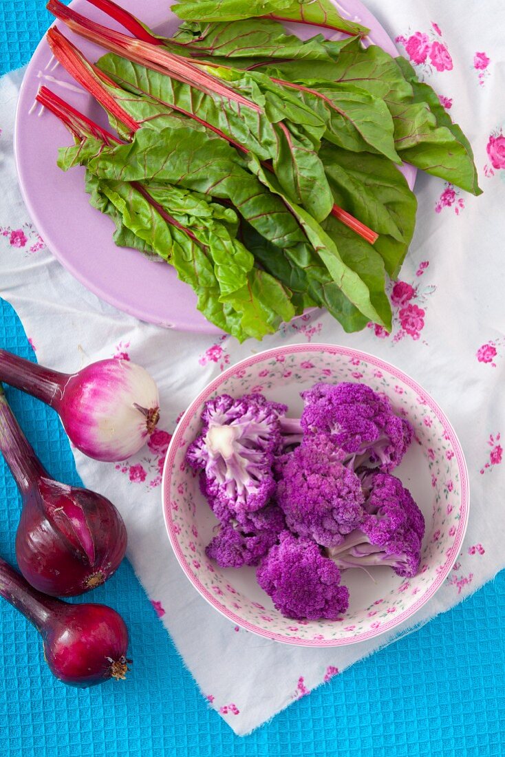 An arrangement of beetroot leaves, red onion and purple cauliflower