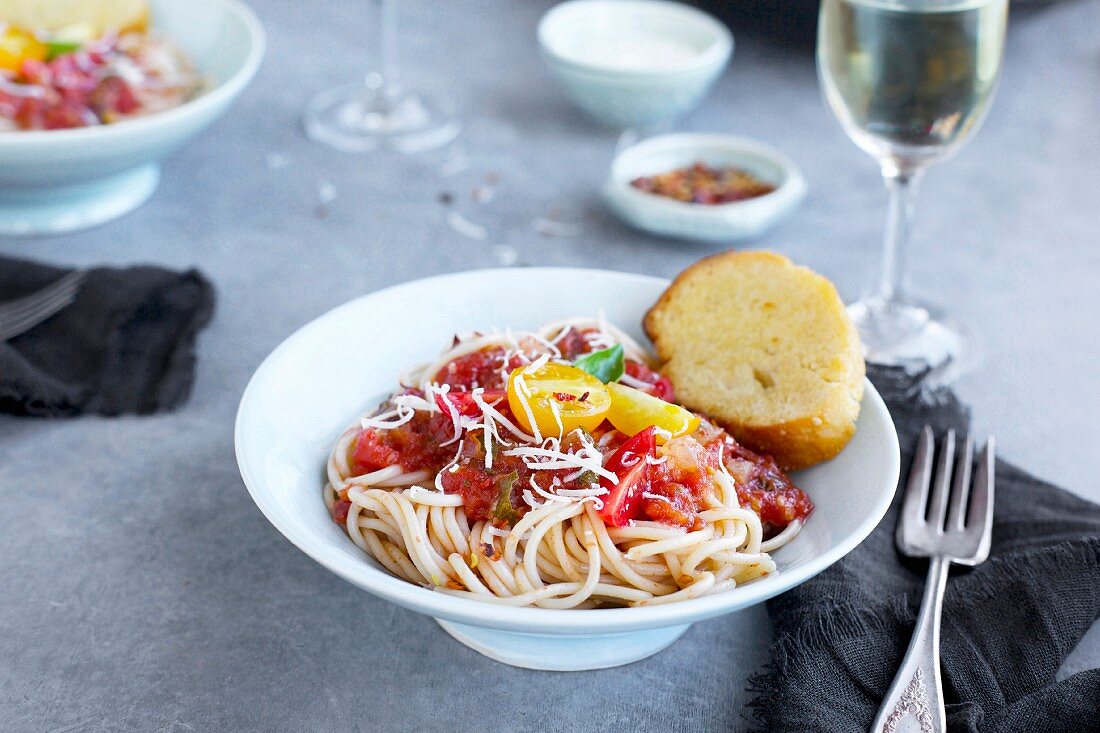 Brauner Reis-Spaghetti mit Tomaten-Basilikum-Sauce, serviert mit Parmesan, Brot und Wein
