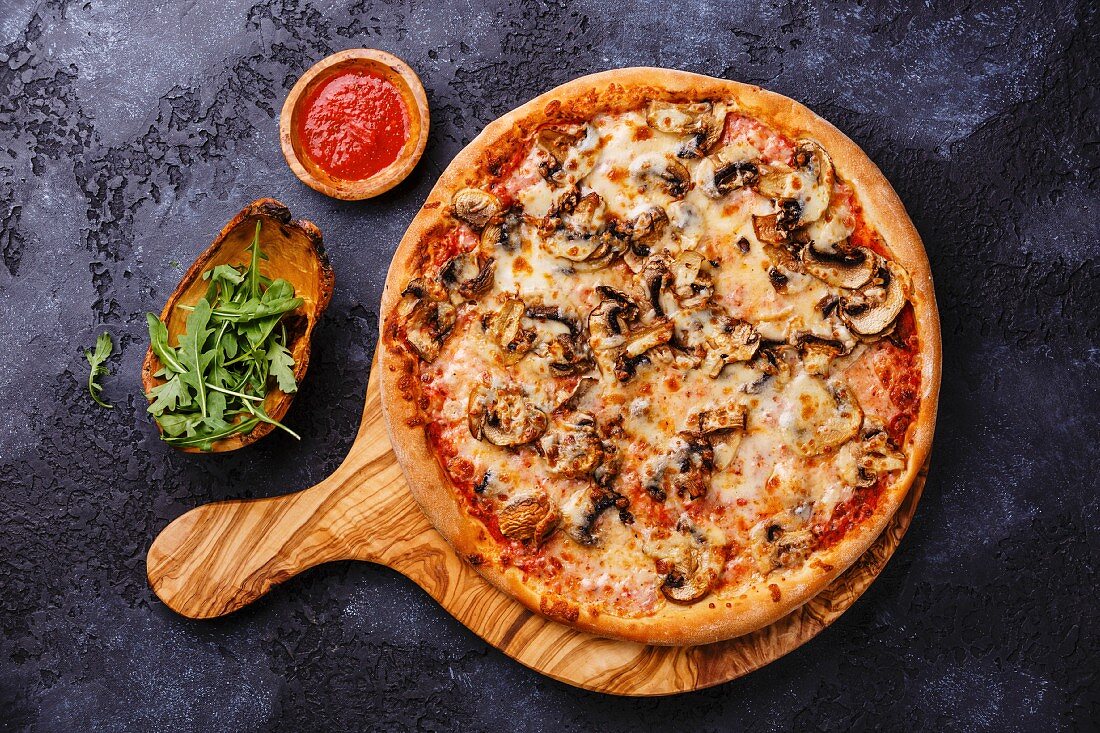 Pizza with mushrooms on wood olive cutting board on dark background