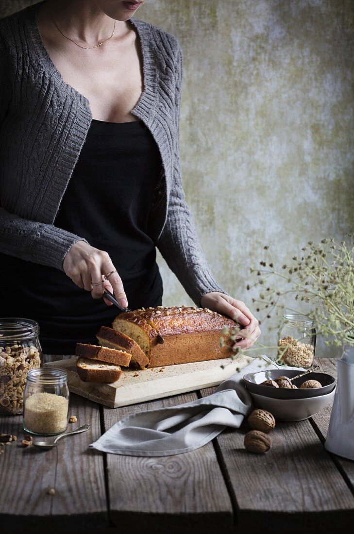 Frau schneidet Müsli-Kuchen auf einem rustikalen Holztisch
