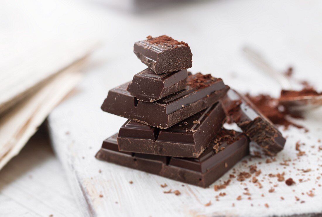 Stacked pieces of chocolate with cocoa powder on a chopping board
