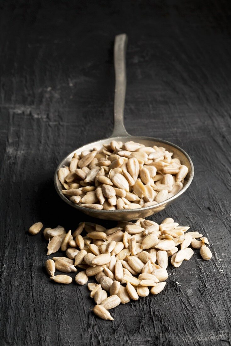 Peeled sunflower seeds on a silver spoon on a black wooden background