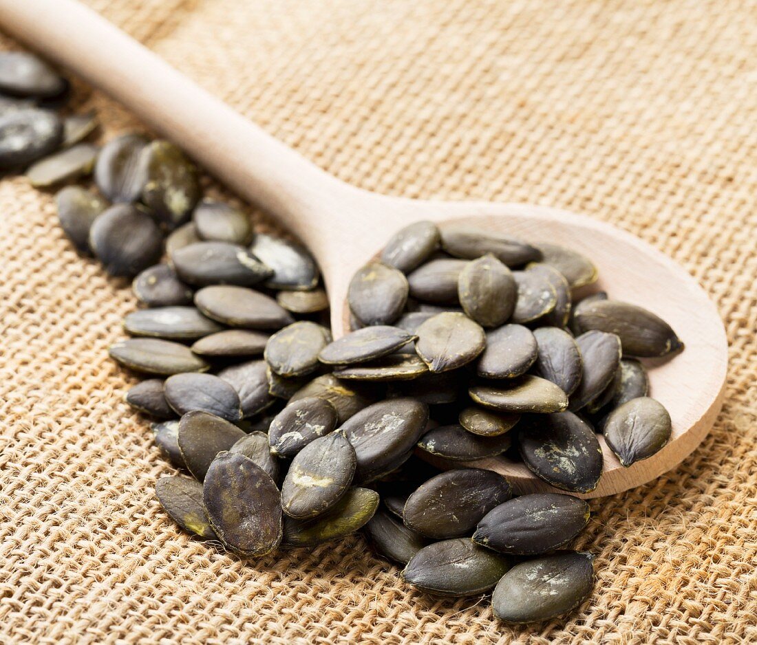 Unpeeled pumpkin seeds on a wooden spoon on a jute sack