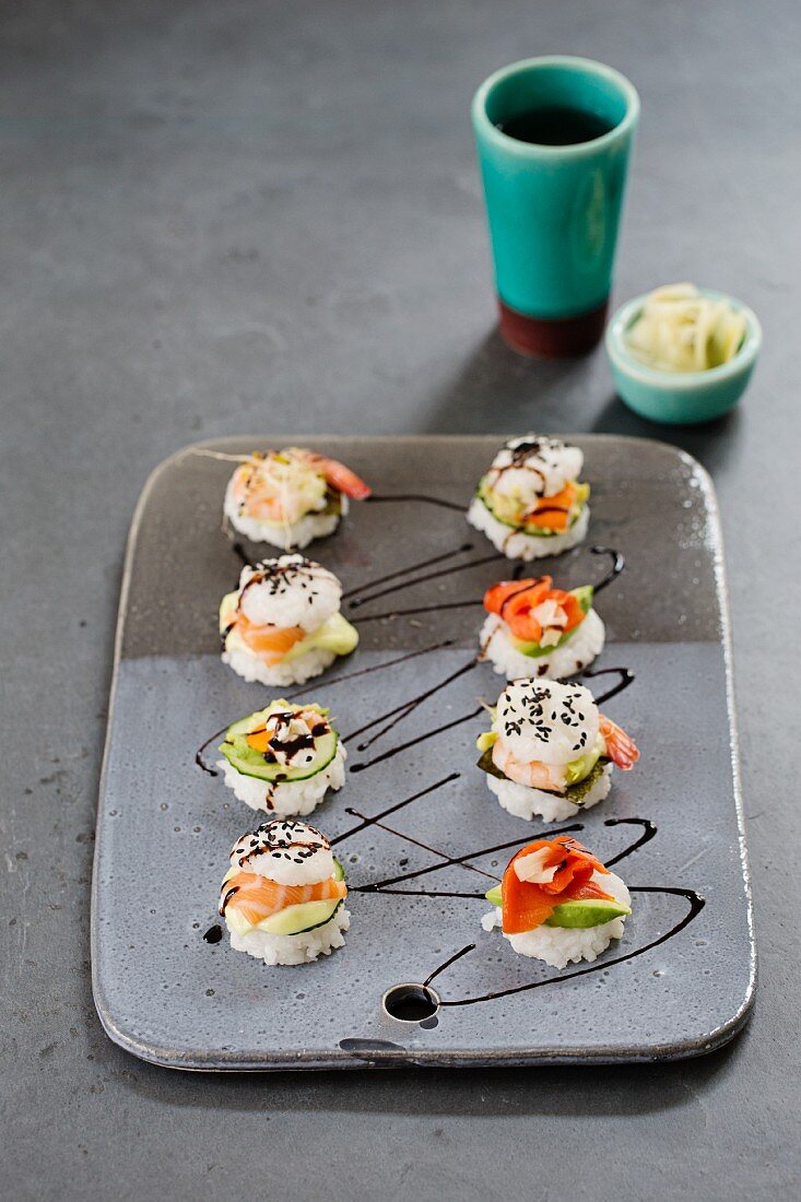 Eight mini sushi burgers on a ceramic plate with smoked and fresh salmon, surimi and shrimp