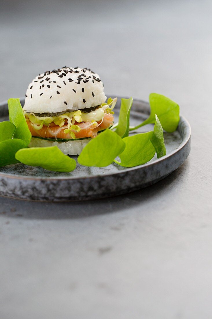 A sushi burger with fresh salmon, cucumber, noris, sprouts, wasabi mayo and purslane