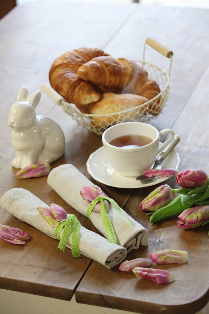 Gerollte Stoffserviette mit Tulpenblütenblättern und grünem Sptizenband auf österlichem Frühstückstisch