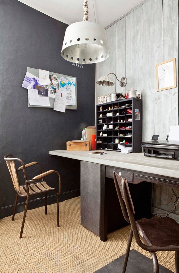 Schreibtisch mit schwarzem Setzkasten vor grauer Holzverkleidung