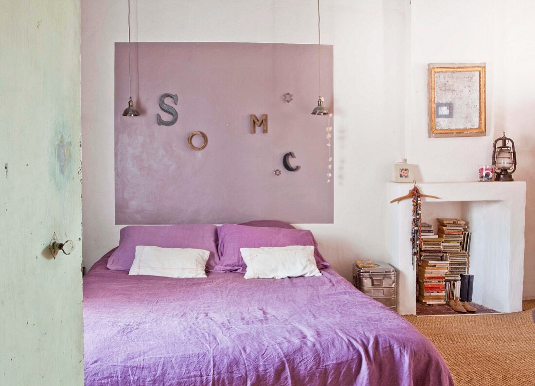 Doppelbett mit lila Bettwäsche und passender Wanddekoration neben stillgelegtem Kamin