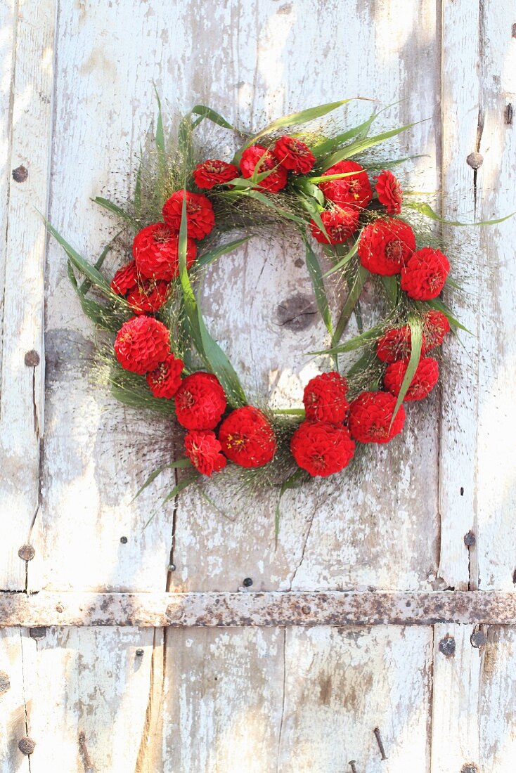 Wreath of red zinnias and switchgrass hung from weathered door