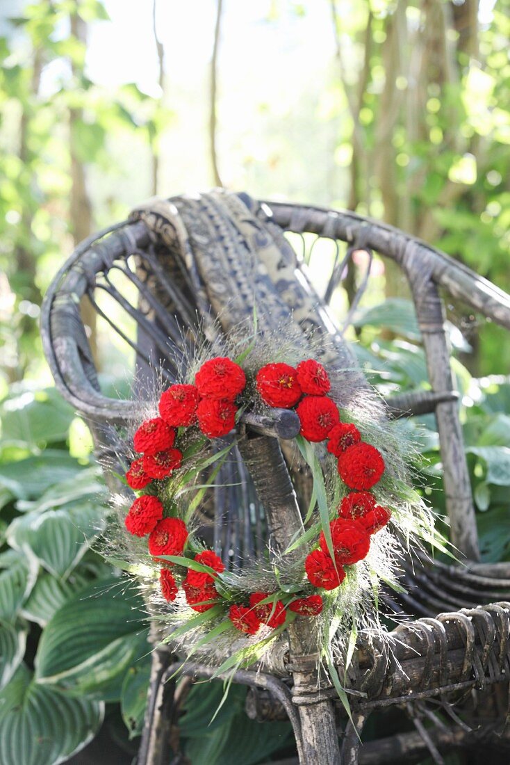 Wreath of red zinnias and switchgrass hung from weathered wicker armchair