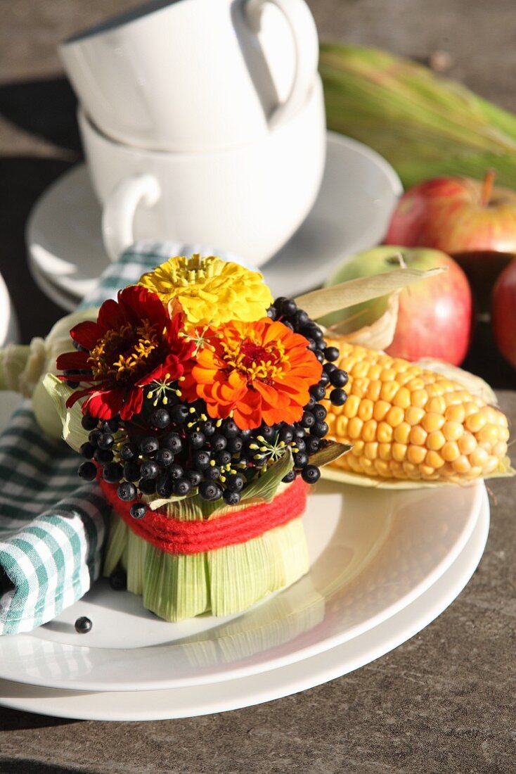 Gesteck aus Zinnienblüten und Hartriegelbeeren, mit Maisblättern drapiert