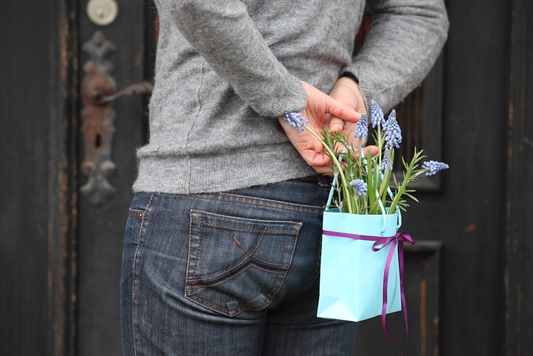 Person holding bag of grape hyacinths behind back
