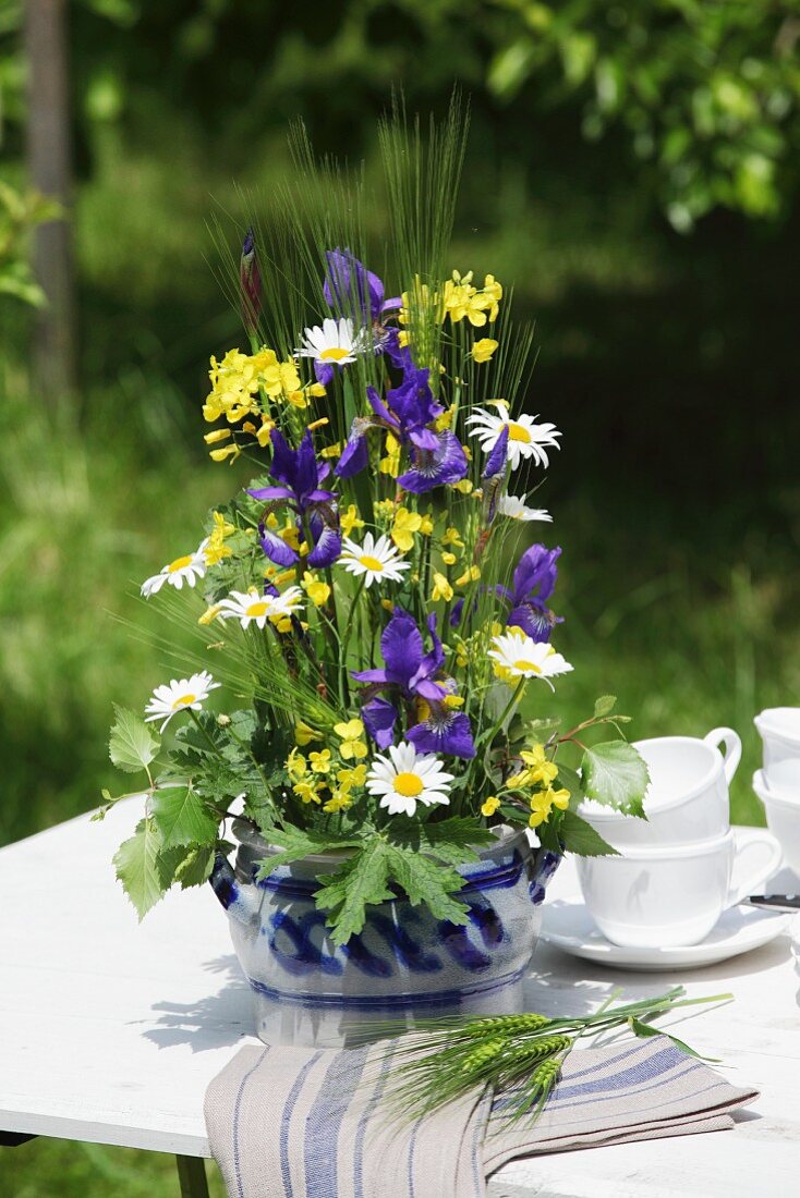Arrangement of iris, rapeseed and ox-eye daisies in stoneware jar