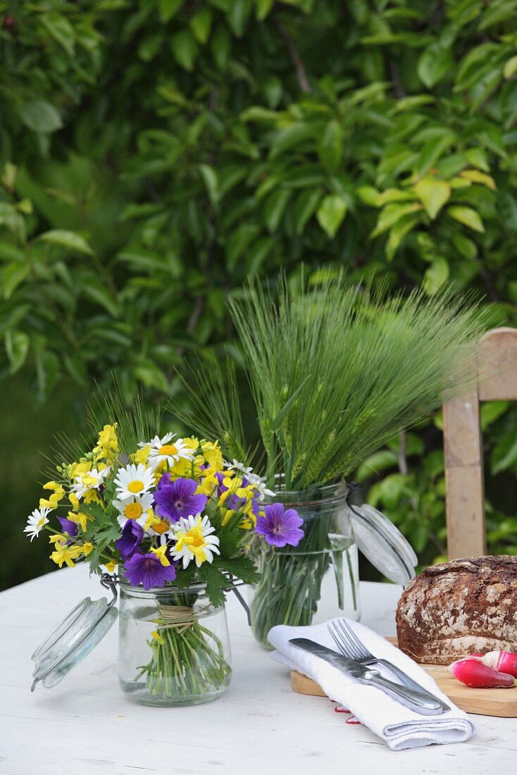 Posies of flowers and green barley in preserving jars on table