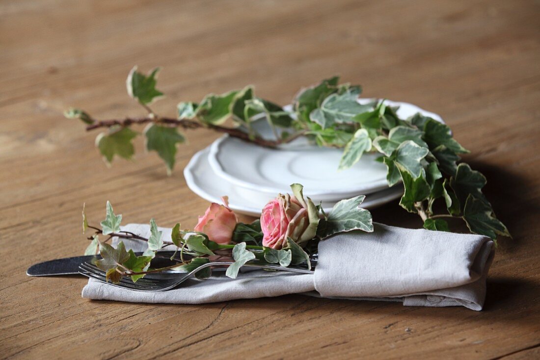 Romantische Tischdekoration mit Rosenblüten und Efeu in Stoffserviette mit Besteck