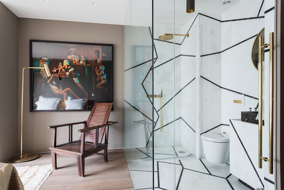 Ensuite bathroom with marble walls, glass partition, framed picture and armchair