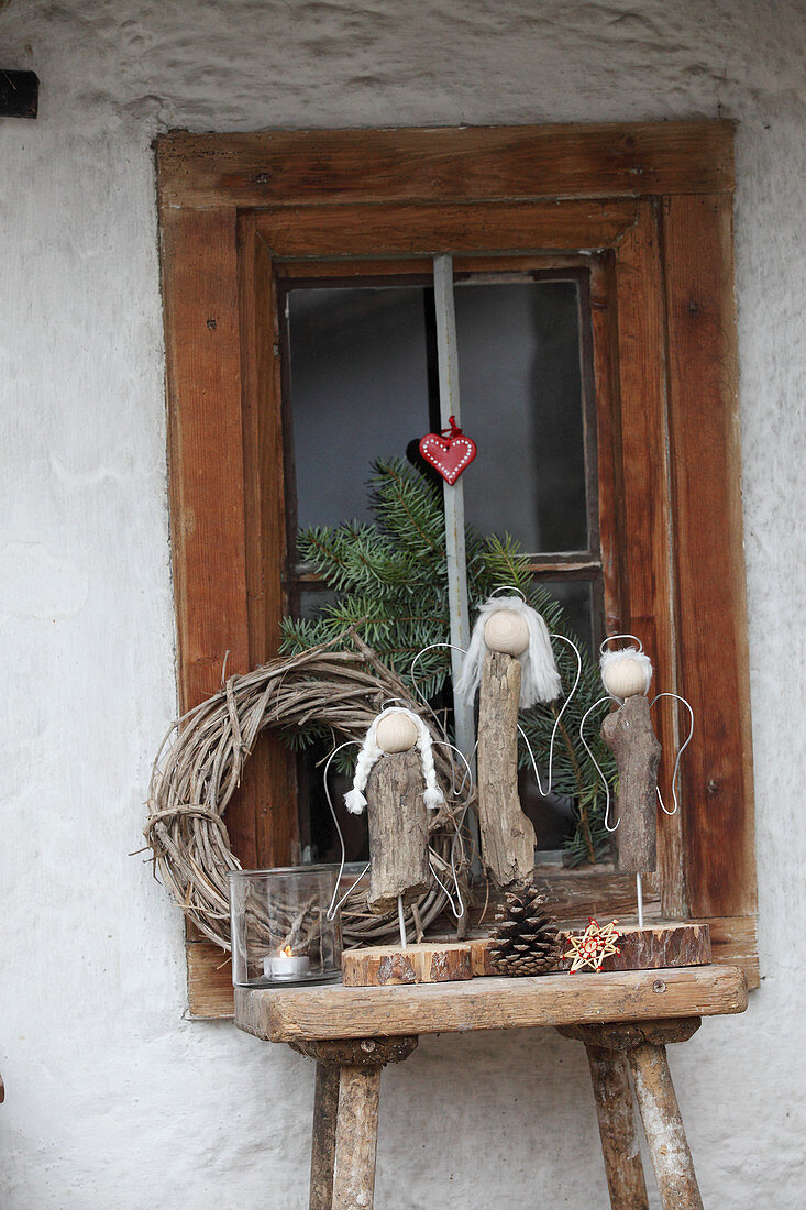 DIY-Engel aus Treibholz auf Holzschemel vor Fenster