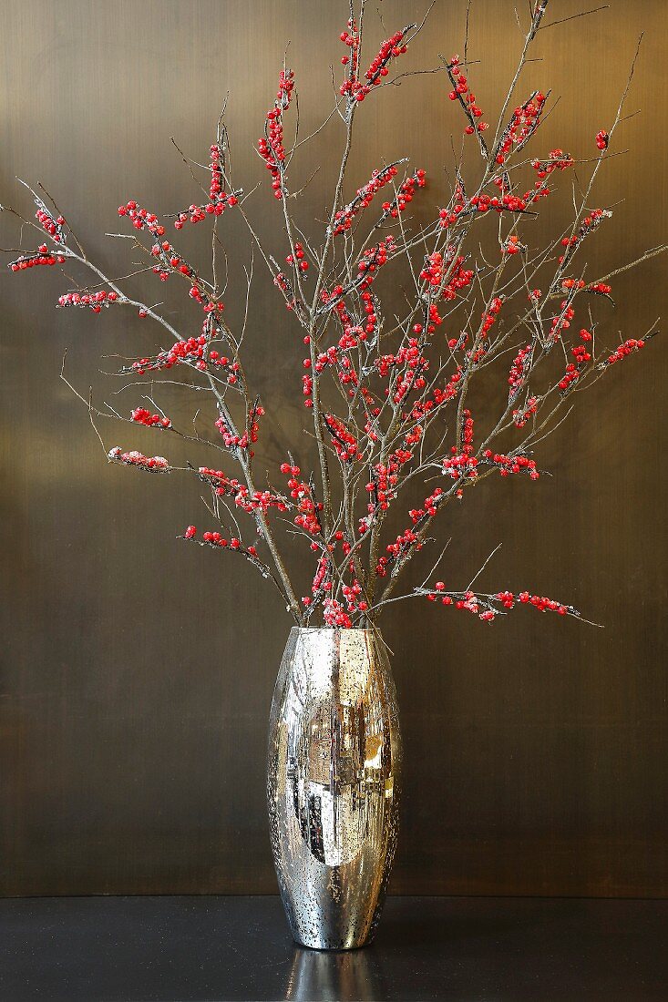 Strauß aus Zweigen mit roten Beeren in einer goldenen Vase