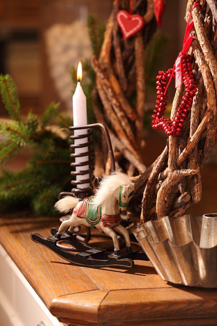Rustikaler Kranz aus Zweigen, Kerze, Schaukelpferdchen und alte Napfkuchenform als Weihnachtsdeko