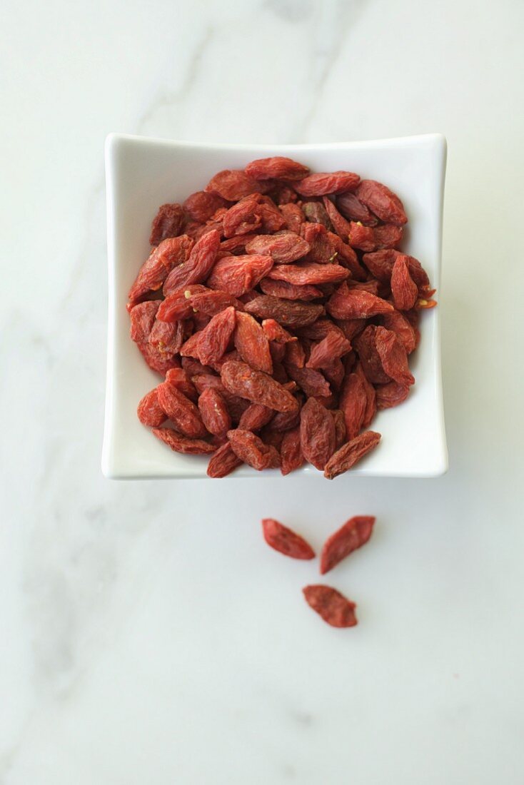 Goji berries in a white bowl on a marble background