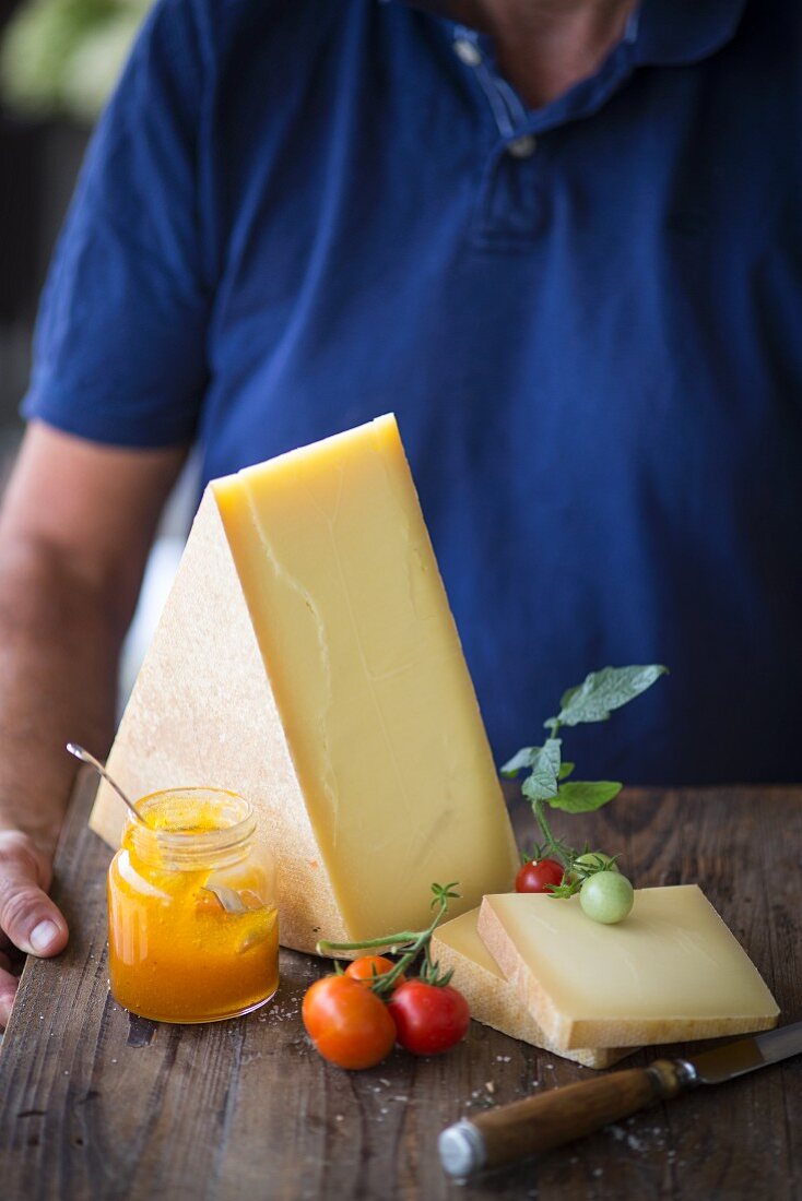 Mann hält Käsebrett mit Marmeladenglas und Tomaten