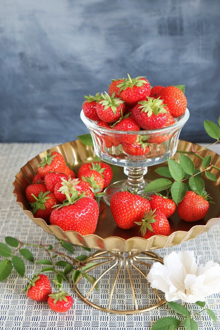 Fresh strawberries in a glass bowl on a white plate with a white paper flower