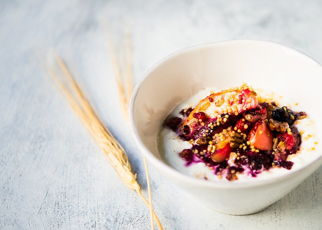 A bowl of Greek yoghurt topped with baked slices of apple with quinoa, oats, pecan nuts and berries
