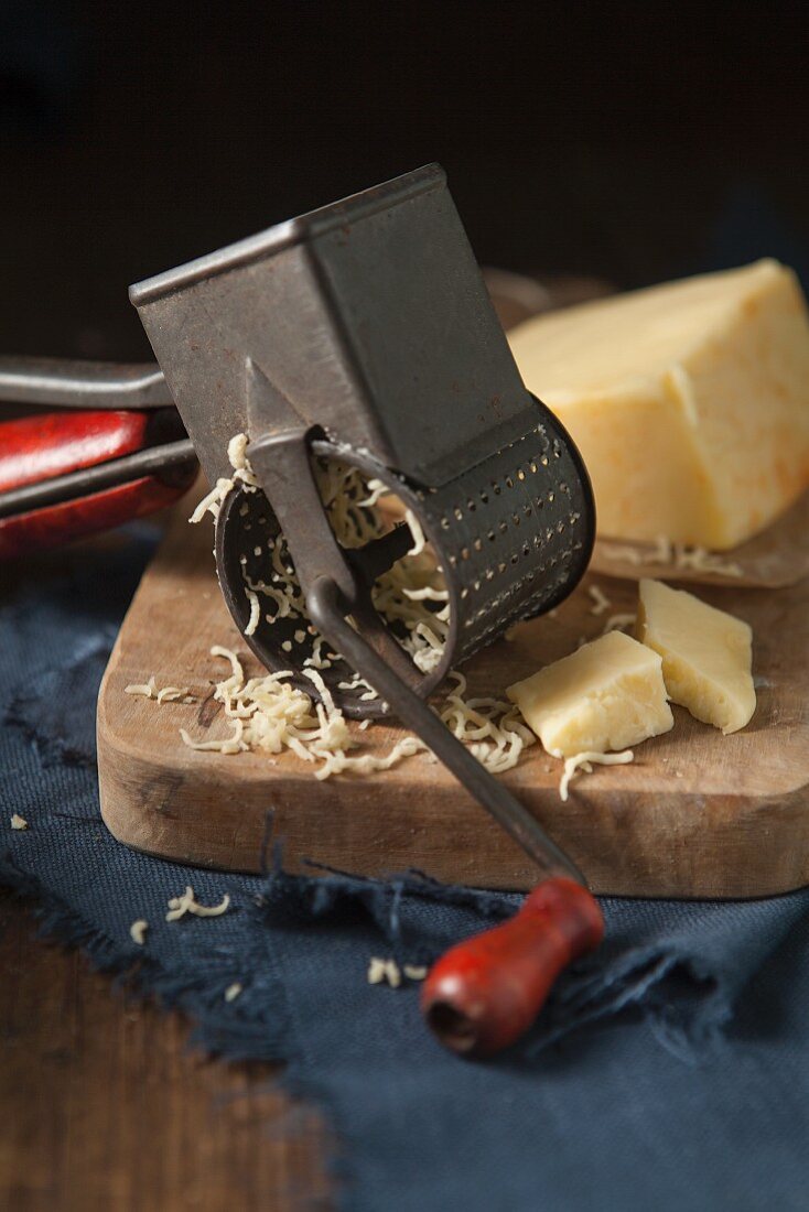 Cheddar auf Holzschneidebrett mit alter Käsereibe