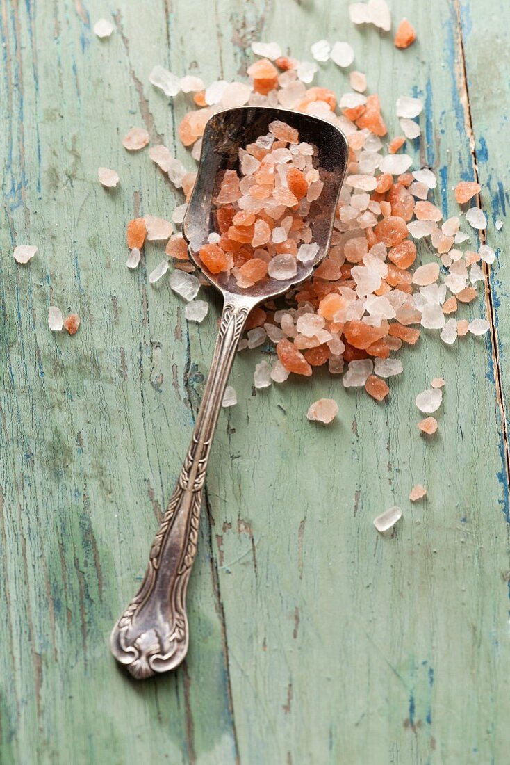 Vinatge silver spoon full of Himalayan pink sea salt on an aqua blue green wooden rustic surface