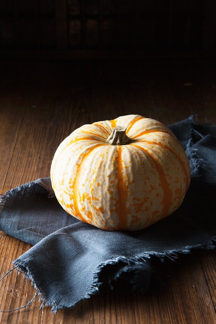 A munchkin pumpkin on a frayed, dark blue linen napkin