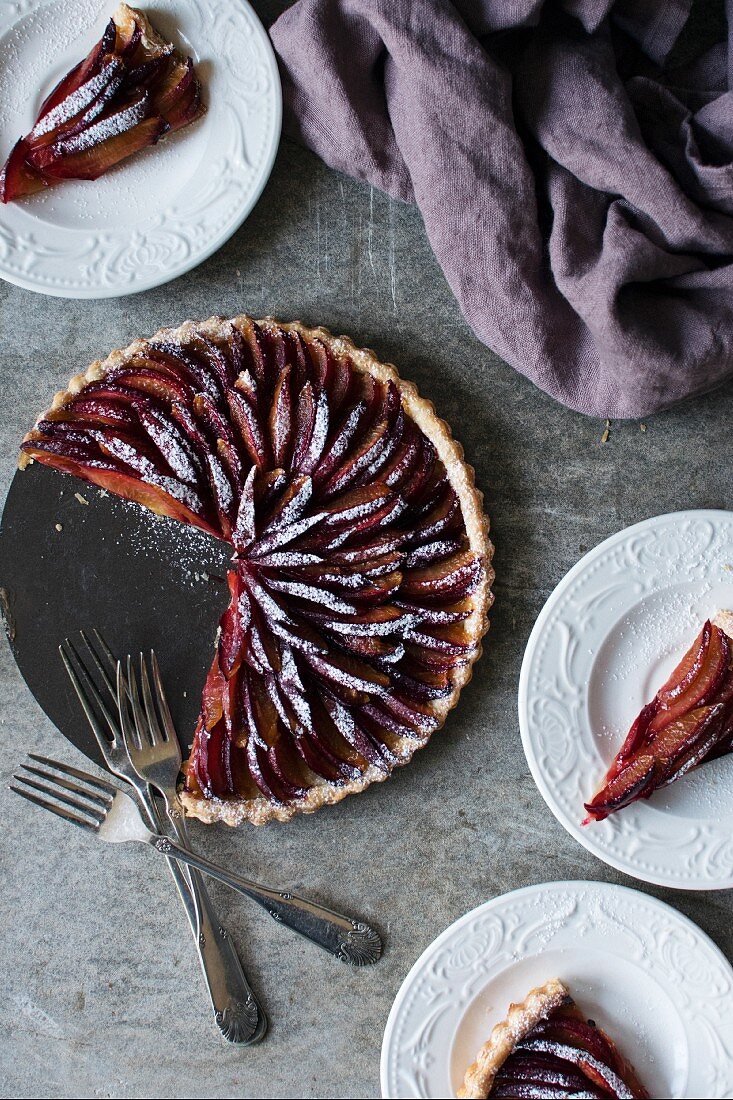 Plum tart dusted in icing sugar with slices cut out