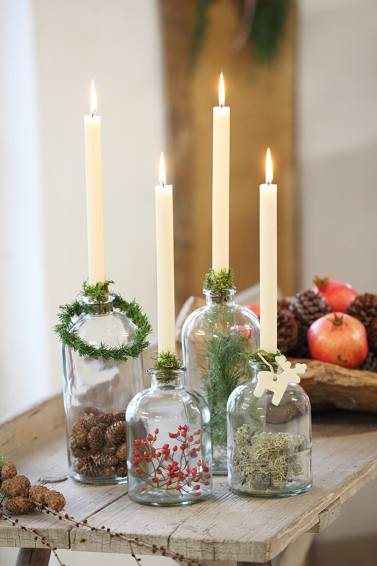 Vier brennende Kerzen in alten Glasflaschen mit Naturdeko darin