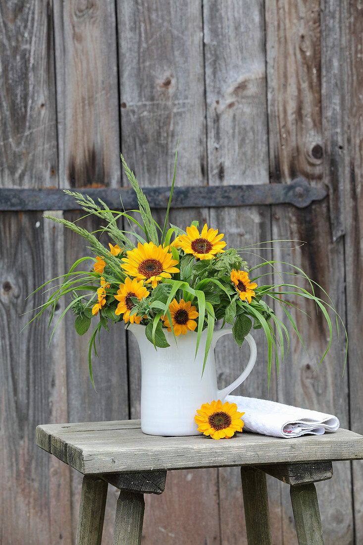 Sunflowers and ornamental grasses in jug on stool
