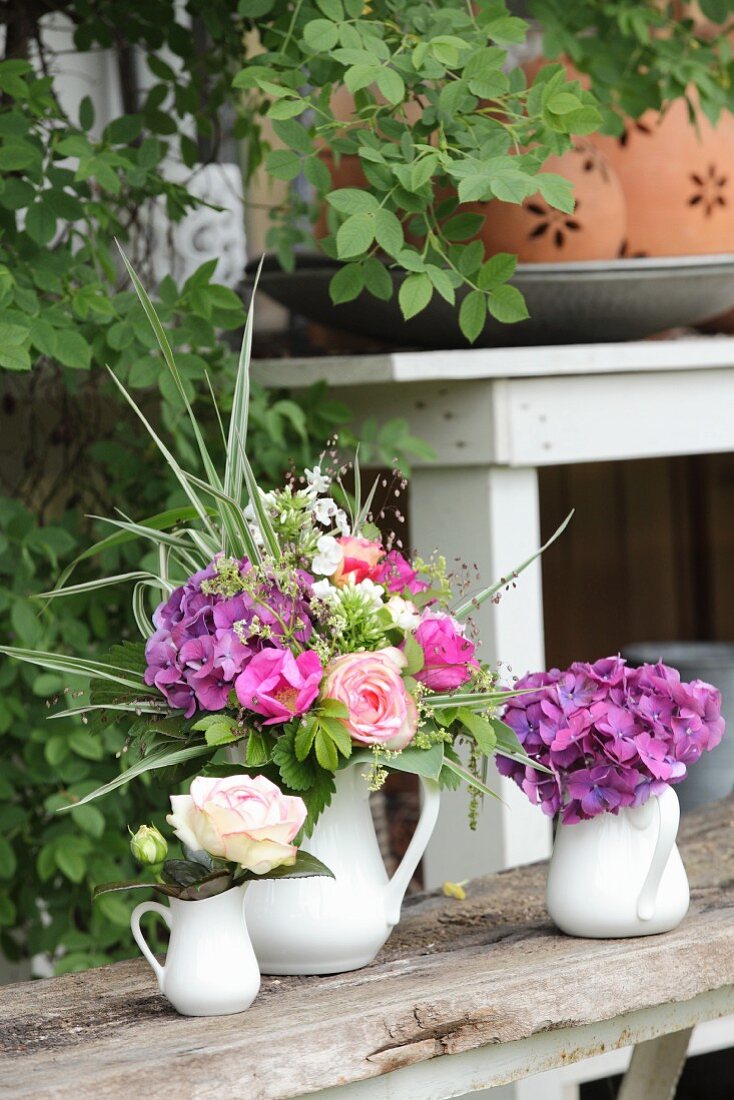 Three jugs holding roses, hydrangeas and a luxuriant summer bouquet