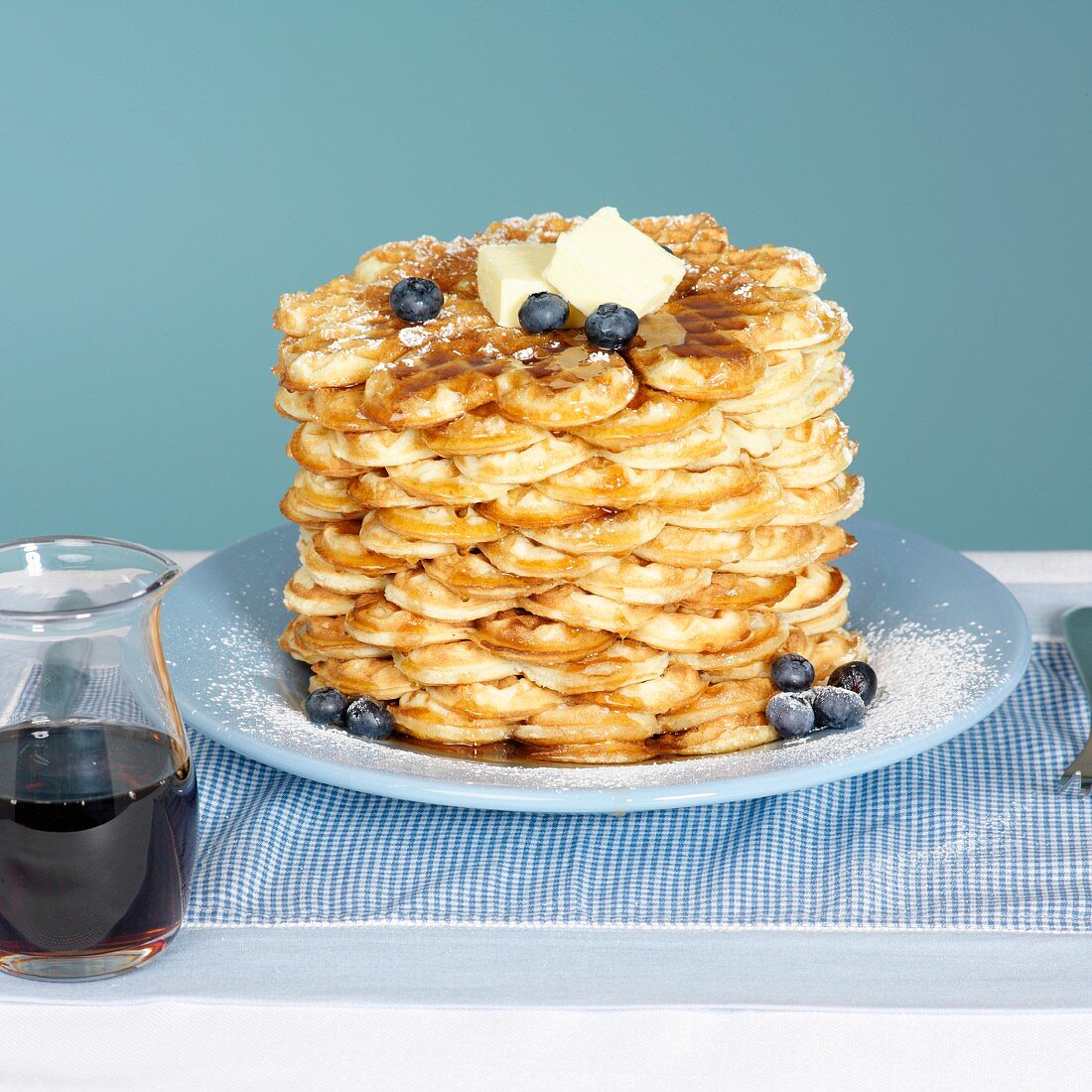 Ein Stapel Waffeln mit Butter, Blaubeeren und Ahornsirup im Krug