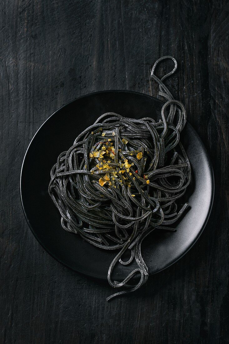 Cooked black pasta with saffron salt over black background