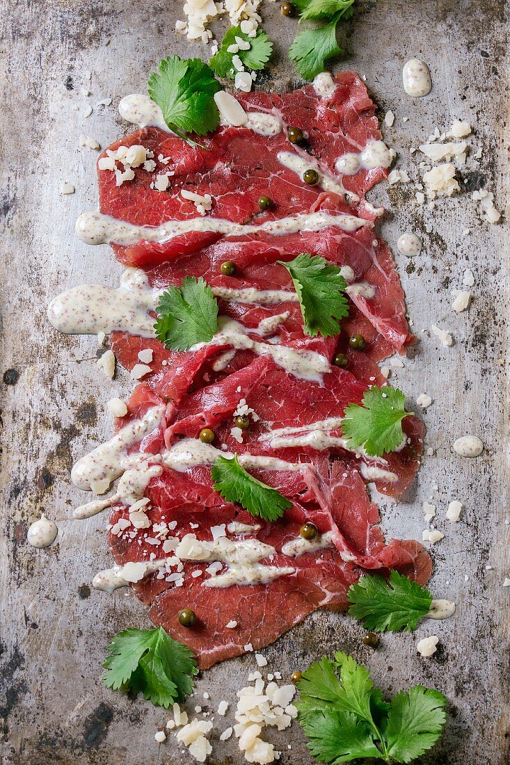 Rindercarpaccio mit Senf-Parmesan-Sauce, Käse, grünem Pfeffer und Koriander