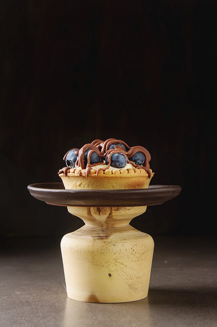 Lemon tartlet, pie, tart with fresh blueberries and milk chocolate on a vintage tray over black background