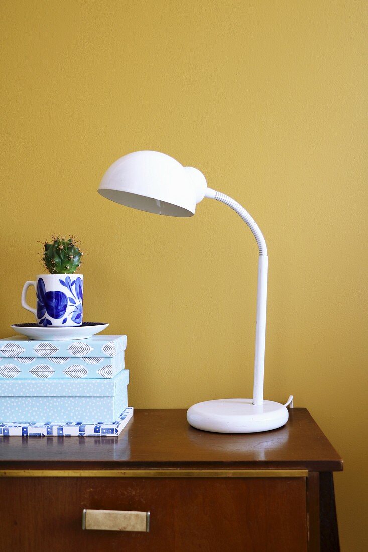 White table lamp next to gift boxes and cactus planted in coffee cup against yellow wall