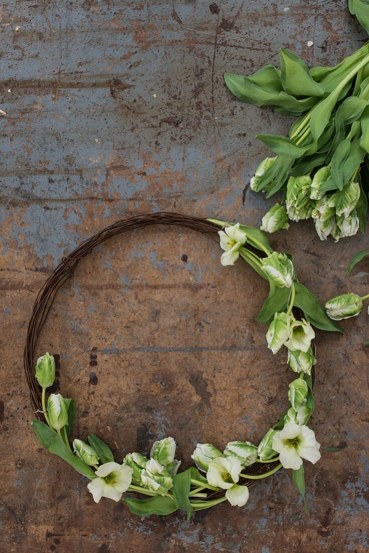 Rustikaler Kranz aus rostigem Draht und Tulpen auf abgenutztem Tisch