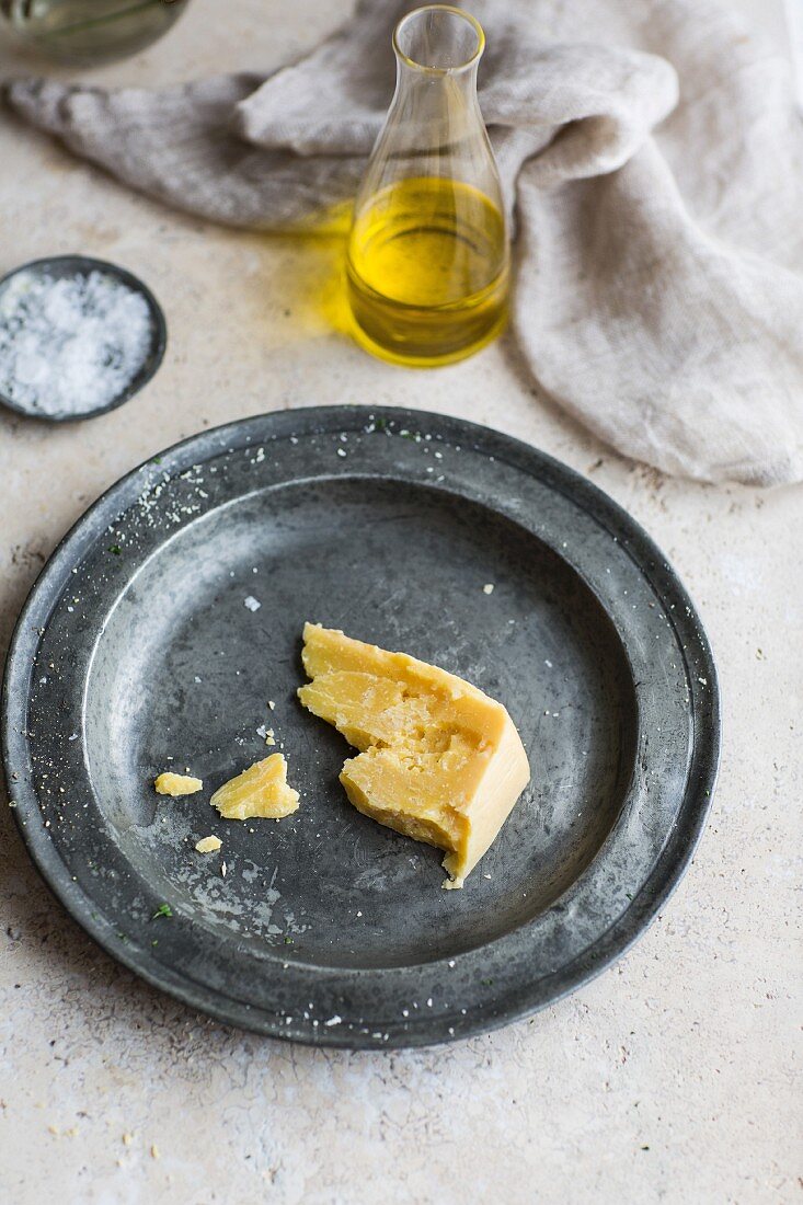A piece of parmesan cheese on a metal plate with olive oil and salt