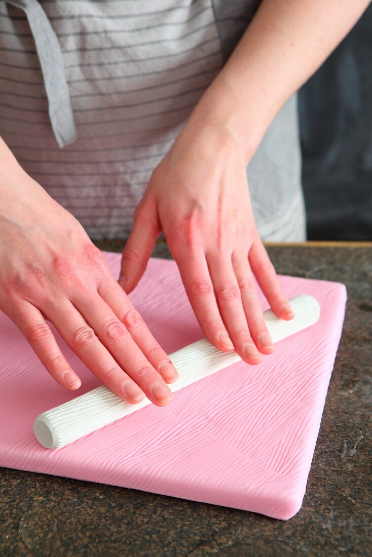 Patterns being rolled into soft fondant icing cake board with a textured rolling pin
