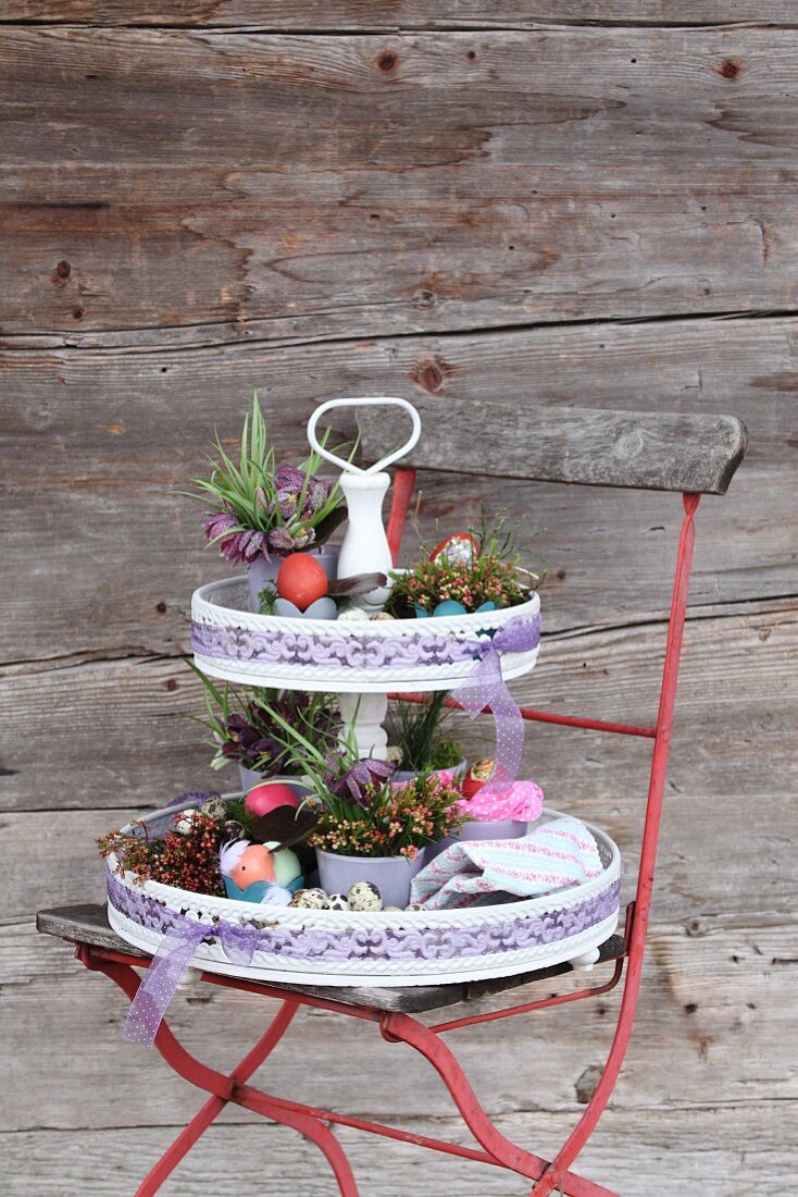 Etagere mit österlicher Blumendeko auf rotem Gartenstuhl