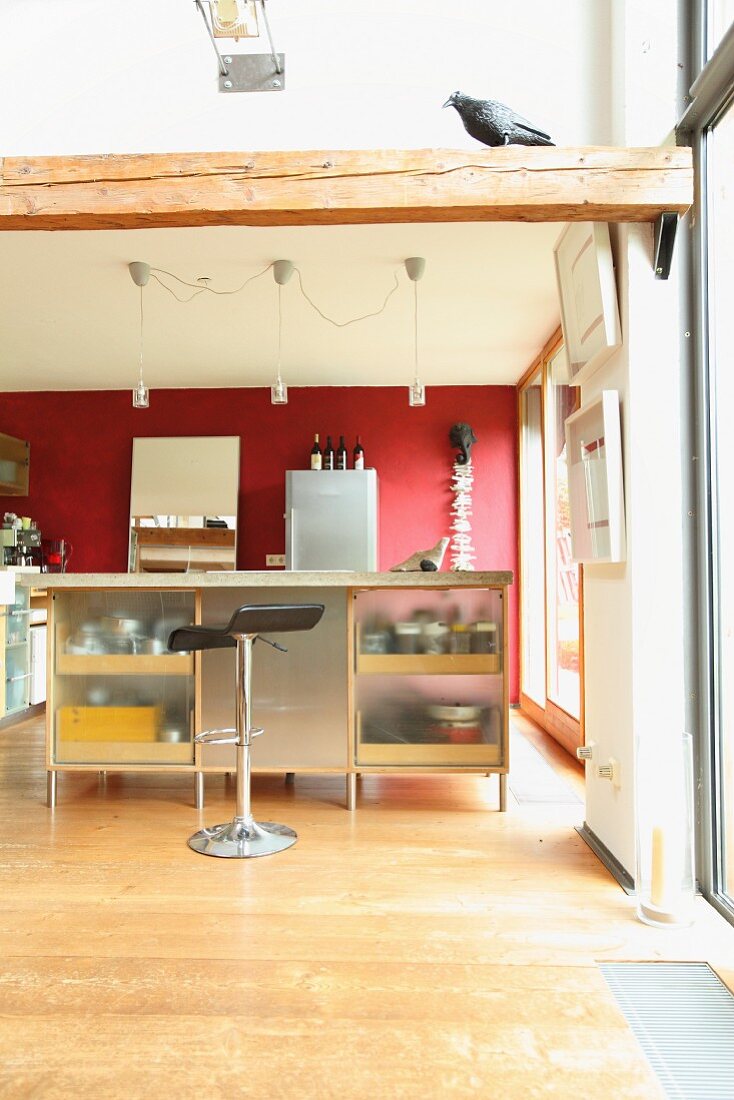 Island counter, bar stools and red wall in open-plan kitchen