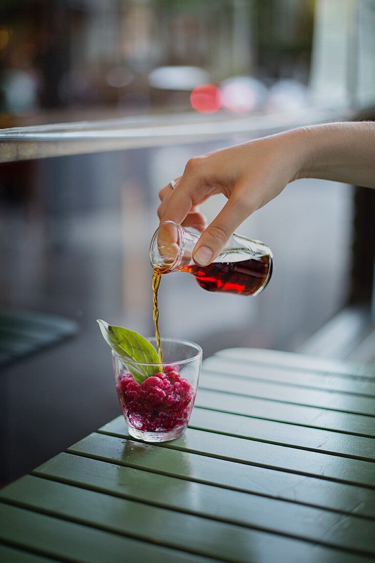 A hand pouring herb liqueur on pomegranate granita in a glass